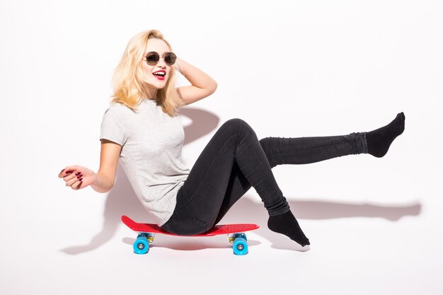 Jeune femme assise sur une planche à roulettes isolée sur un mur blanc.