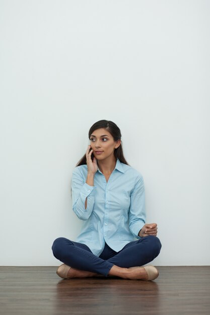 Jeune femme assise sur le plancher et sur appel téléphonique