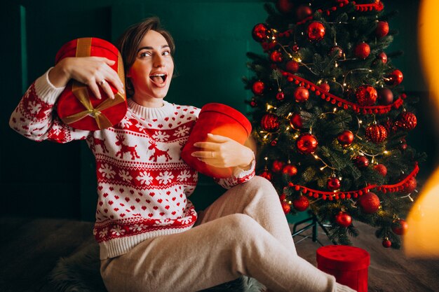 Jeune femme assise près du sapin de Noël avec des boîtes rouges