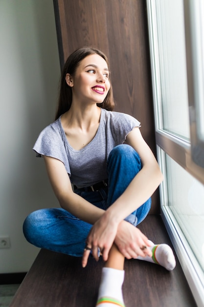 Photo gratuite jeune femme assise sur un rebord de fenêtre près de la fenêtre avec vue sur la ville le matin.