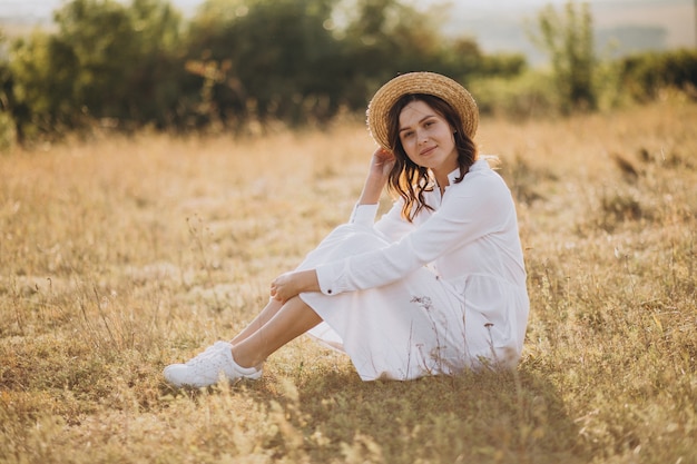 Jeune femme assise en robe blanche et chapeau sur le terrain