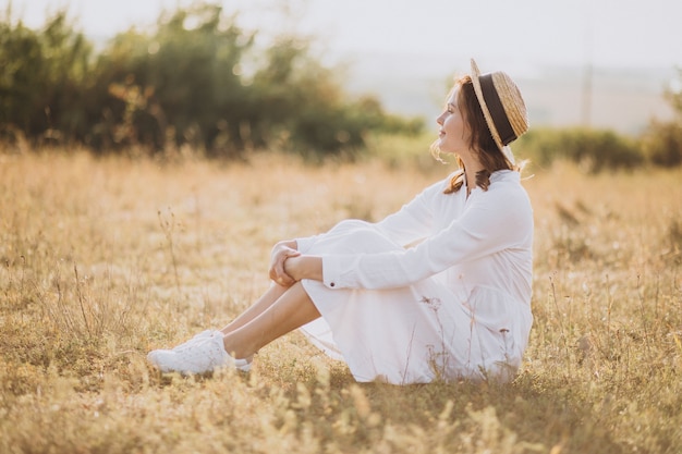 Jeune femme assise en robe blanche et chapeau sur le terrain