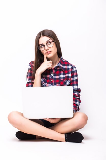 Une jeune femme assise sur le sol avec un ordinateur portable sur blanc