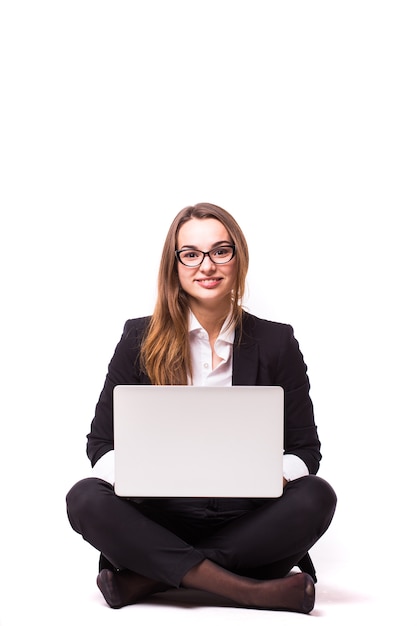 Jeune femme assise sur le sol et utilisant un ordinateur portable isolé sur un mur blanc