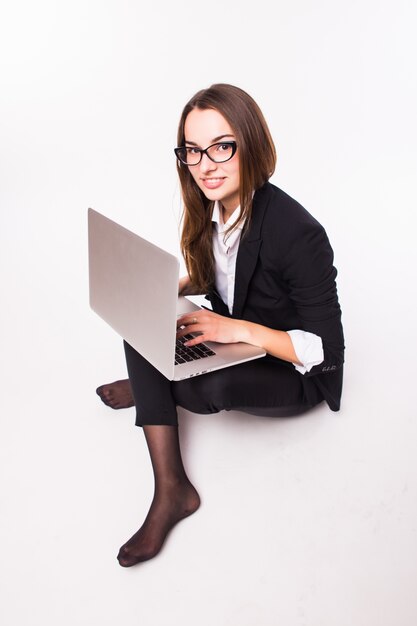 Jeune femme assise sur le sol et utilisant un ordinateur portable isolé sur un mur blanc