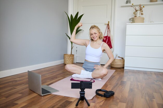Une jeune femme athlète, instructrice de fitness, s'assoit sur un tapis en caoutchouc et enregistre une vidéo sur numérique.