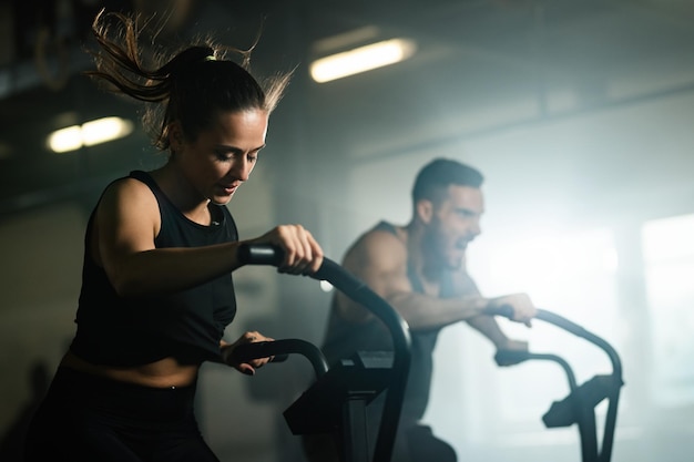 Jeune femme athlétique ayant un entraînement croisé sur un vélo stationnaire dans une salle de sport