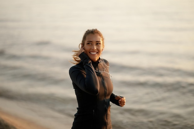 Jeune femme athlétique heureuse courant au bord de la mer et écoutant de la musique sur des écouteurs