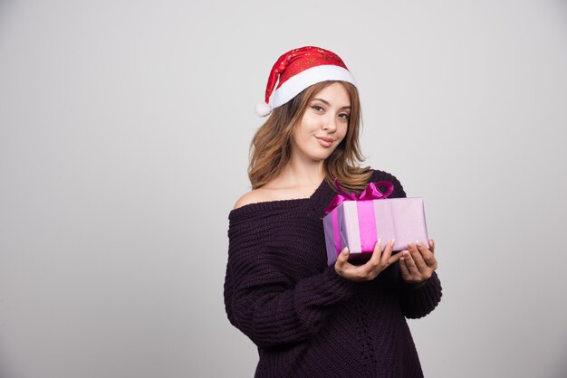 Jeune femme au bonnet de Noel tenant une boîte-cadeau présente.