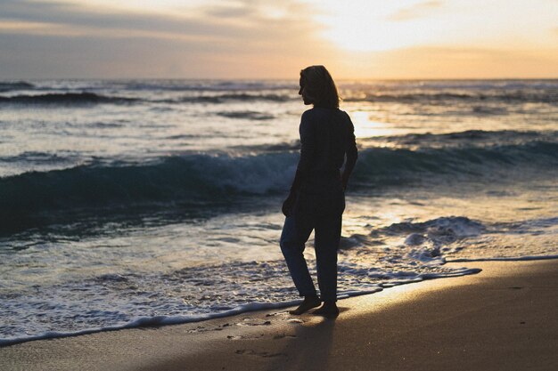 Jeune femme au bord de l'océan au coucher du soleil.