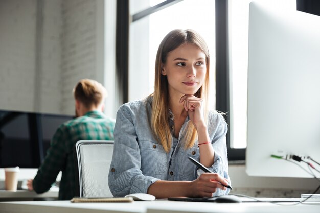 Jeune femme au bureau à l'aide d'un ordinateur et d'une tablette graphique