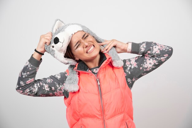 Jeune femme au chapeau drôle sur un mur blanc.