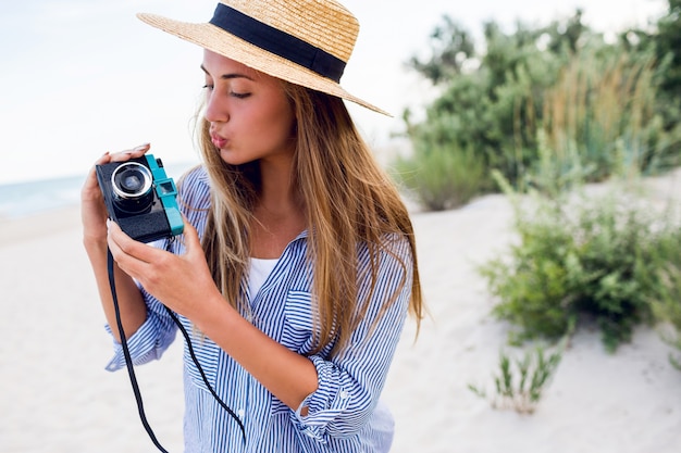 Jeune femme au chapeau de paille faisant photo avec appareil photo rétro sur la plage