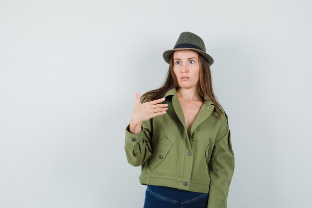 Jeune femme au chapeau de pantalon de veste pointant sur elle-même et à la perplexité