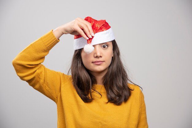 Jeune femme au chapeau rouge du père Noël posant sur un mur blanc.