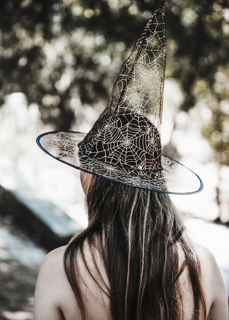 Jeune femme au chapeau de sorcière debout dans la forêt