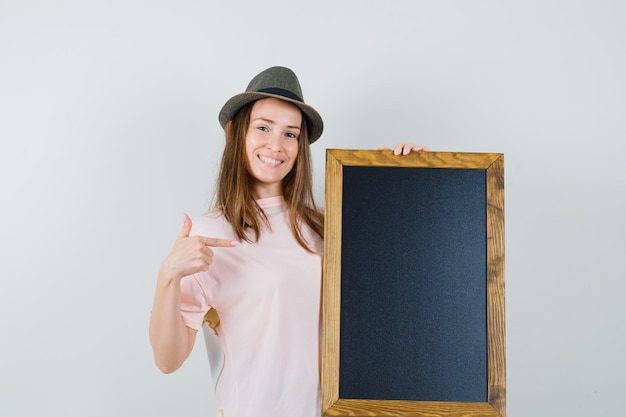 Jeune femme au chapeau t-shirt rose pointant sur tableau noir et à la joyeuse