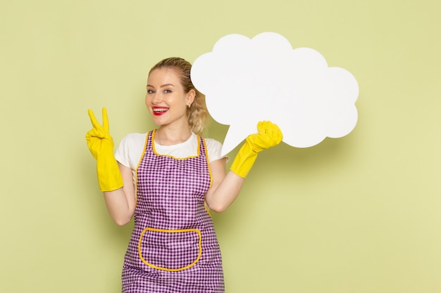 Jeune femme au foyer en chemise et cape violette avec des gants jaunes tenant grand panneau blanc sur vert