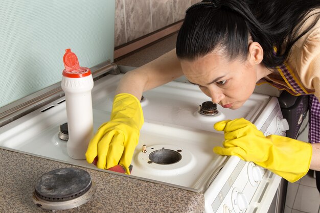 Jeune femme au foyer avec des gants jaunes nettoyage cuisinière à gaz
