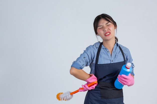 Jeune femme au foyer porte des gants jaunes lors du nettoyage avec le produit de nettoyage sur mur blanc.