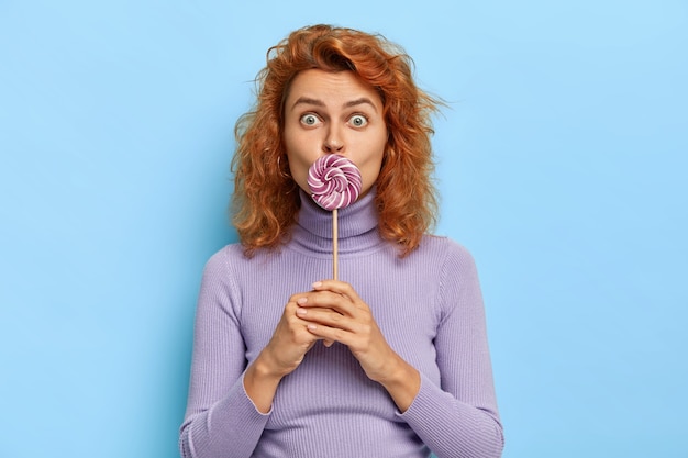 Jeune femme au gingembre tient une sucette sur la bouche