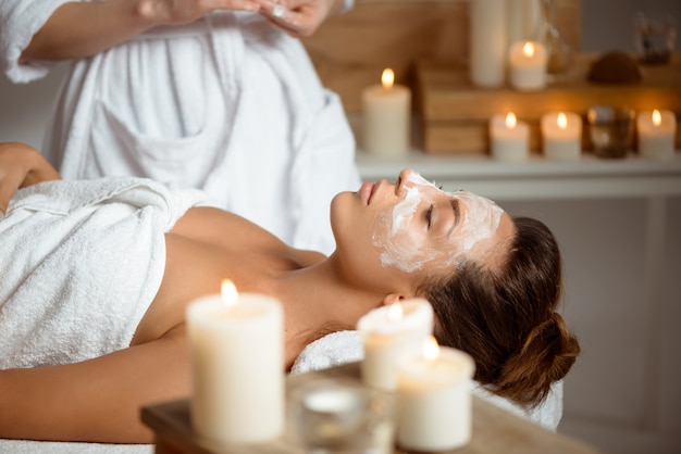 Jeune femme au masque pour le visage relaxant dans le salon spa.