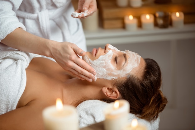 Jeune femme au masque pour le visage relaxant dans le salon spa.