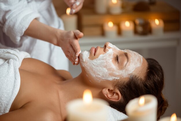 Jeune femme au masque pour le visage relaxant dans le salon spa.