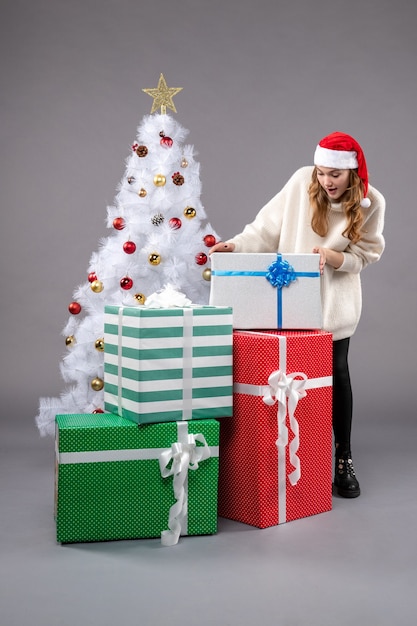 Jeune femme autour de cadeaux de Noël sur un sol gris près de l'arbre de Noël