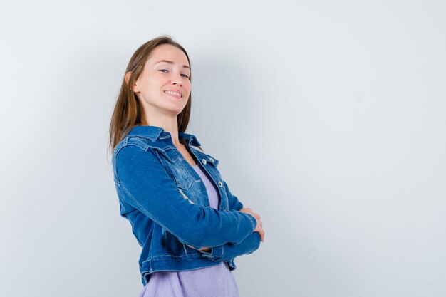 Jeune femme aux bras croisés en veste en jean et à la fierté. vue de face.