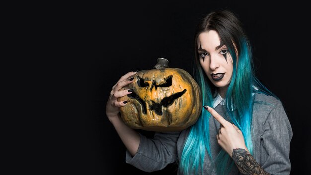 Jeune femme aux cheveux bleus pointant vers la citrouille d&#39;Halloween