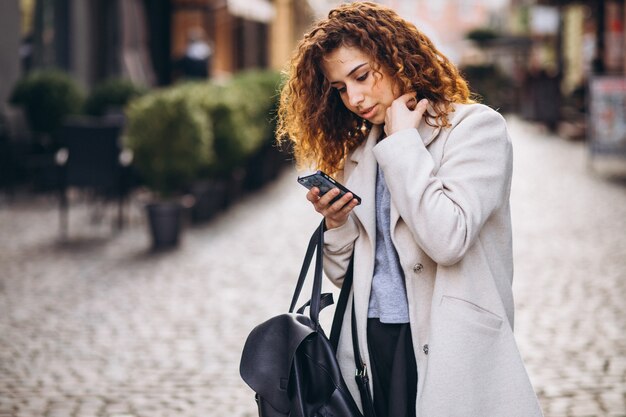 Jeune femme aux cheveux bouclés à l'aide de téléphone à la rue