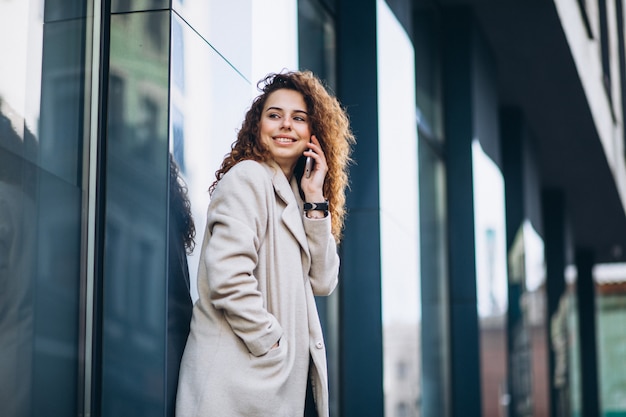 Jeune femme aux cheveux bouclés à l'aide de téléphone à la rue