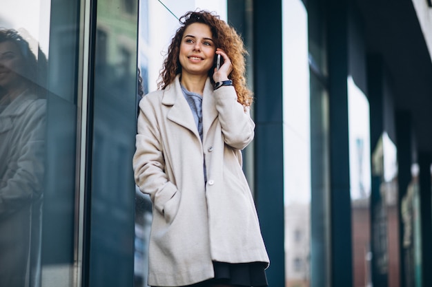 Jeune femme aux cheveux bouclés à l'aide de téléphone à la rue