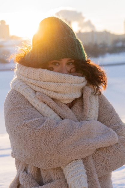 Jeune femme aux cheveux bouclés foncés dans un chapeau d'hiver, chaudement vêtue, gelée d'hiver, journée ensoleillée à l'extérieur.