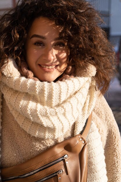 Jeune femme aux cheveux bouclés noirs, manteau de fourrure chaudement habillé, écharpe, gelée d'hiver, journée ensoleillée dans la rue de la ville.