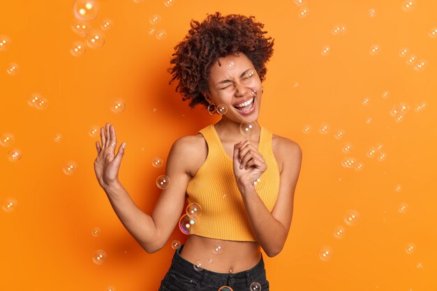 Jeune femme aux cheveux bouclés ravie chante la chanson garde la main comme si le microphone soulève la paume