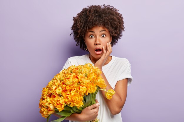 Jeune femme aux cheveux bouclés tenant le bouquet de fleurs jaunes