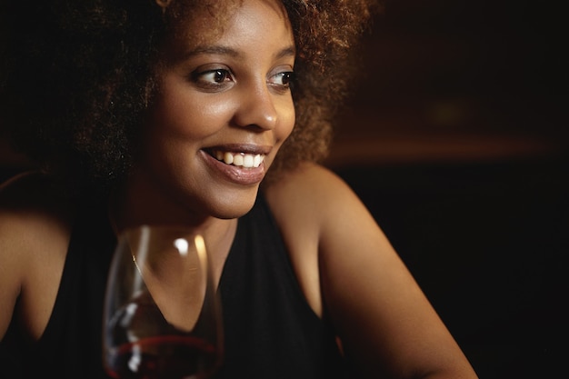 Photo gratuite jeune femme aux cheveux bouclés et un verre de vin rouge