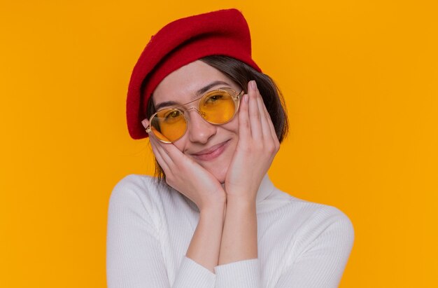 Jeune femme aux cheveux courts en col roulé blanc portant béret et lunettes de soleil jaunes