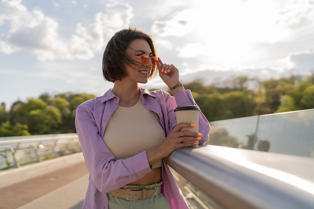 Jeune Femme Aux Cheveux Courts En Tenue D'été élégante, Boire Du Café Sur Le Pont Moderne De Thr