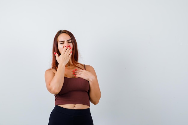 Jeune femme aux cheveux longs dans un crop top marron le bâillement