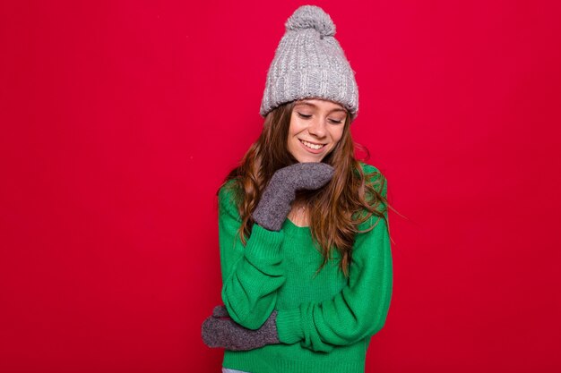 Jeune femme aux cheveux longs en pull vert et bonnet tricoté gris rire sur rouge