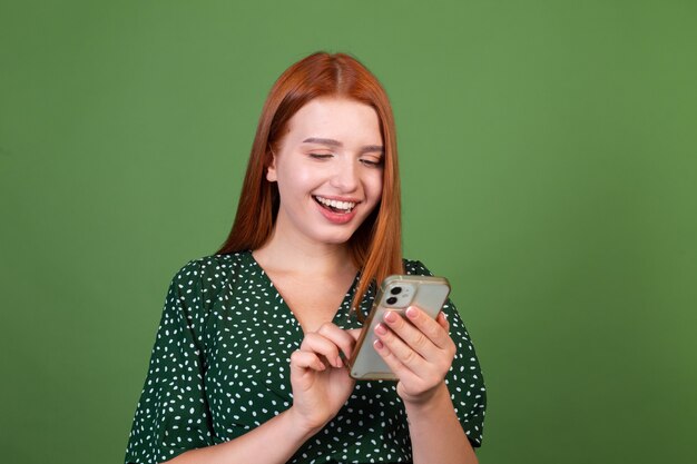 Jeune femme aux cheveux roux sur mur vert avec téléphone portable heureux positif excité