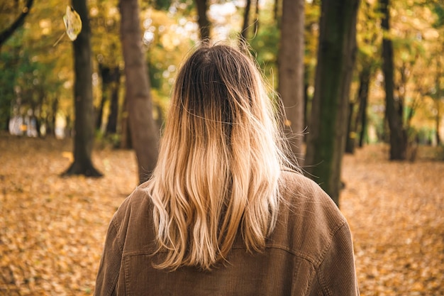 Photo gratuite une jeune femme aux cheveux teints dans la forêt d'automne vue de l'arrière