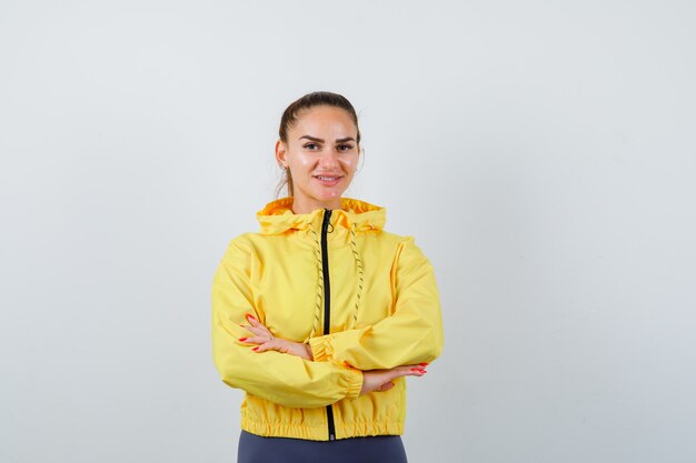 Jeune femme aux mains croisées en veste jaune et à la gaieté, vue de face.