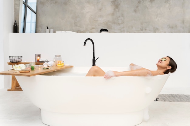 Jeune Femme Ayant Du Concombre Sur Les Yeux Se Relaxant Dans La Baignoire Remplie D'eau Et De Mousse Photo Premium