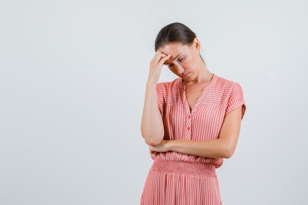 Jeune femme ayant mal à la tête en robe rayée et à la fatigue. vue de face.