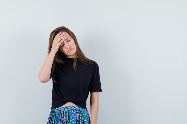 Jeune femme ayant mal à la tête en t-shirt noir et jupe bleue et à la fatigue