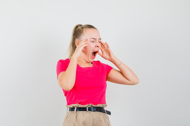 Jeune femme bâillant en t-shirt, pantalon et à la vue de face, somnolent.